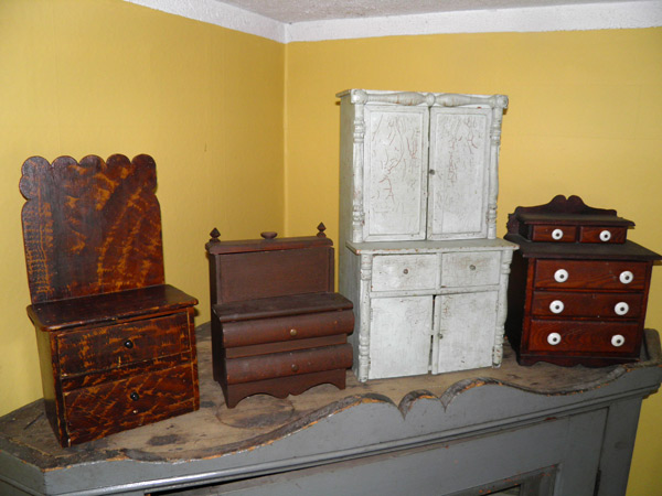 From left to right: a miniature chest of drawers with scalloped backboard (16”H / 8.5 W/ 6”D) from Renfrew County; a sewing stand,  (10”H / 6”W / 4” D) from Western Ontario; white child’s china cupboard (24”H / 13”W / 9”D) from Renfrew County; chest of drawers with original porcelain knobs (13”H / 8.5”W /12”D) from Eastern Ontario. Photo courtesy of Shaun Markey