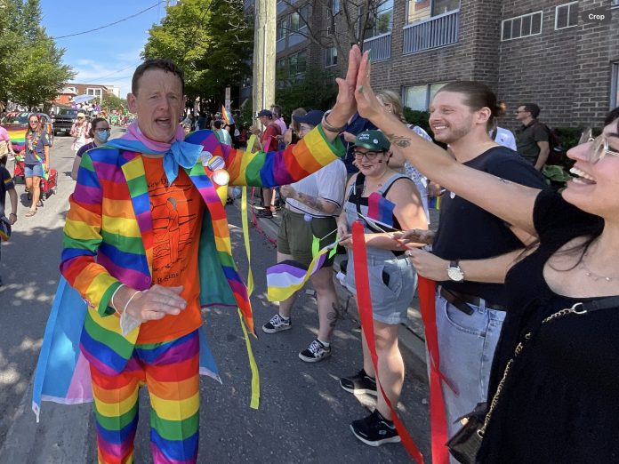 Joel is wearing a rainbow suit. He gives someone a high five on the parade route.