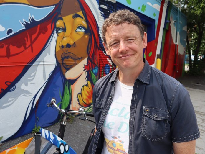 Joel poses for a photo next to a colourful mural.