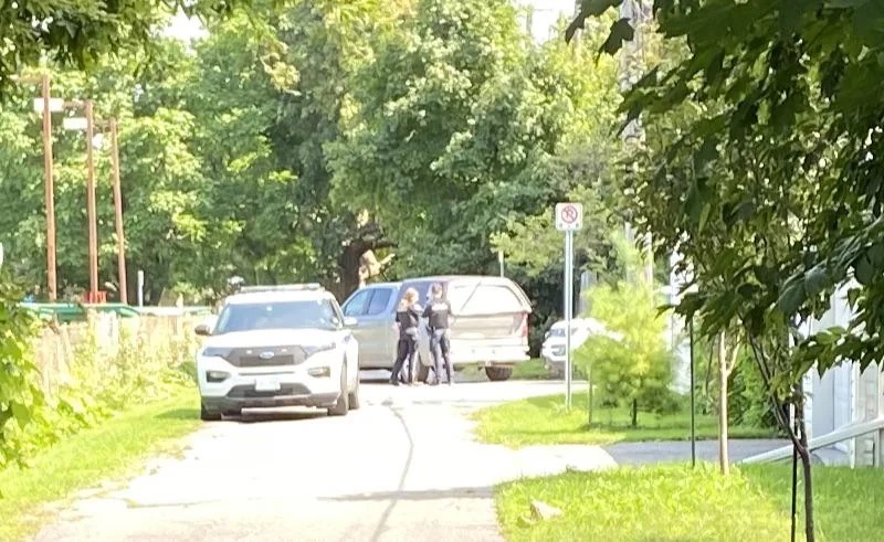 A police car and two officers are seen near a van that is parked in an alleyway. 