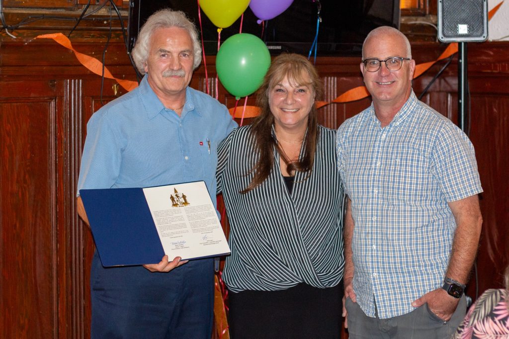 Three people pose for a photo. One of them is holding a certificate.