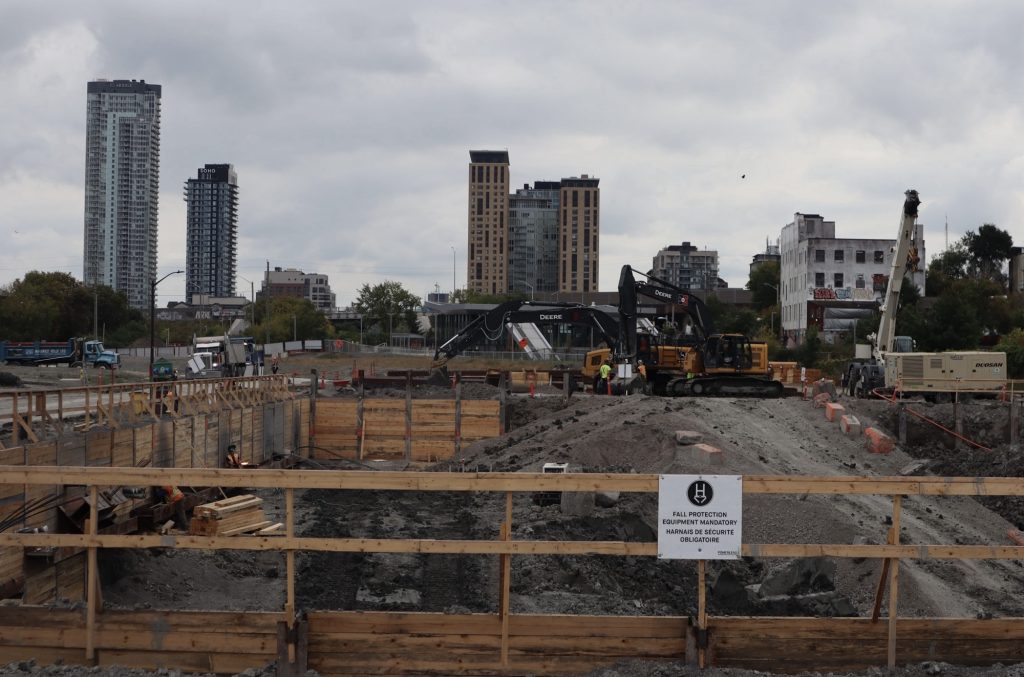 Construction crews in a very large hole. The Preston Street high rise is seen in the distance.