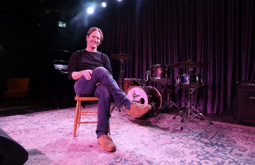 Geoff sits in a chair on a stage.