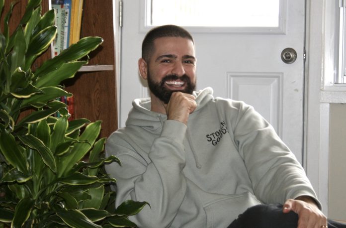 Jordan sits on a chair and poses for a photo. A plant is seen on the left.