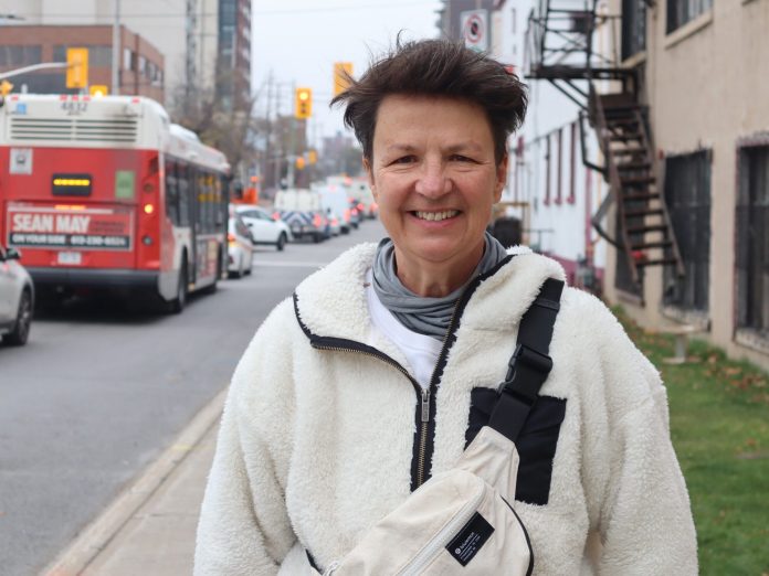 Catherine stands on Parkdale near the Carleton Tsgern. An OC Transpo bus passes by.