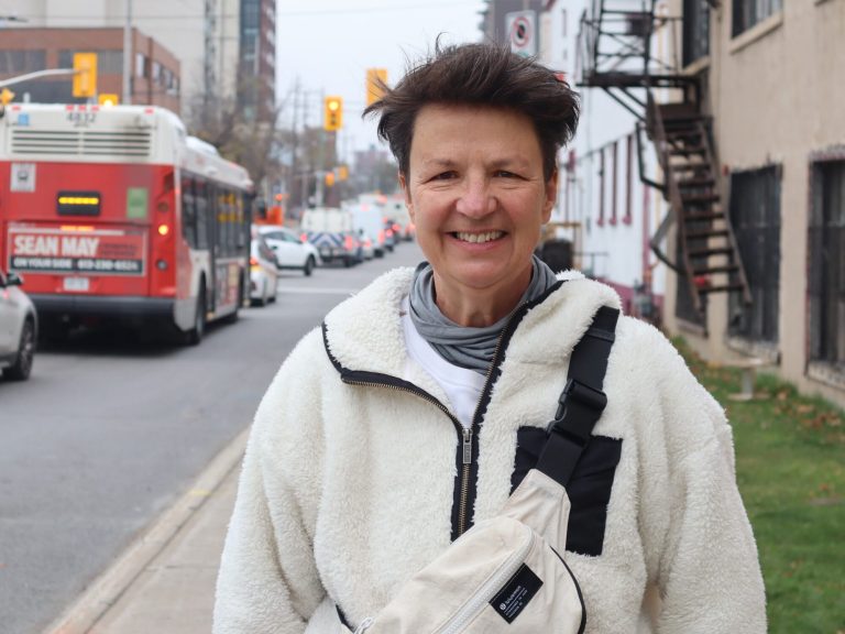 Catherine stands on Parkdale near the Carleton Tsgern. An OC Transpo bus passes by.