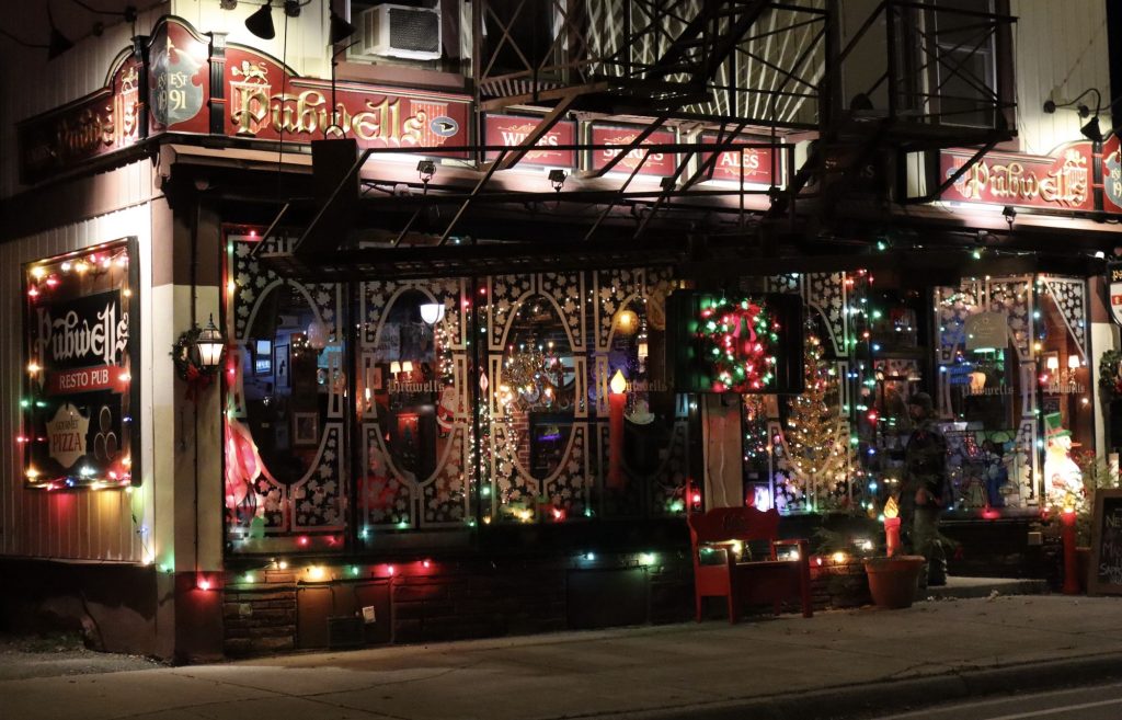 Many Christmas lights of all colours are strung along windows outside of the pub.